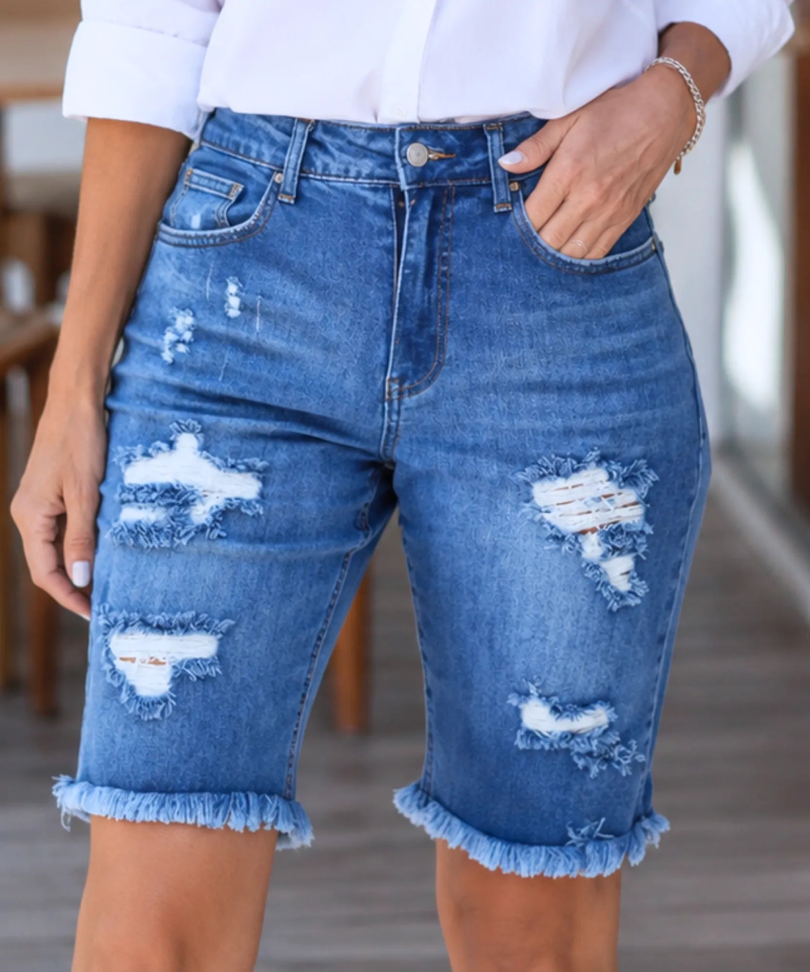 Detalhe dos rasgos frontais da bermuda jeans feminina azul escuro destroyed cintura alta