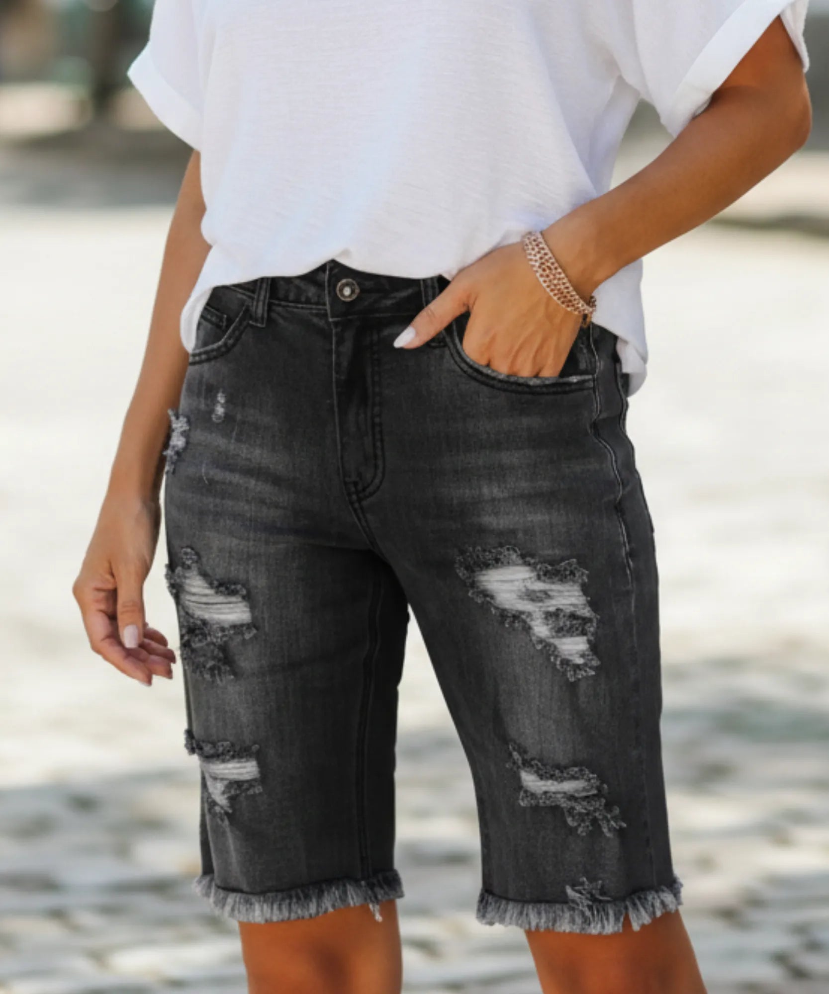 Bermuda jeans feminina preta destroyed com rasgos e barra desfiada, vista frontal do produto