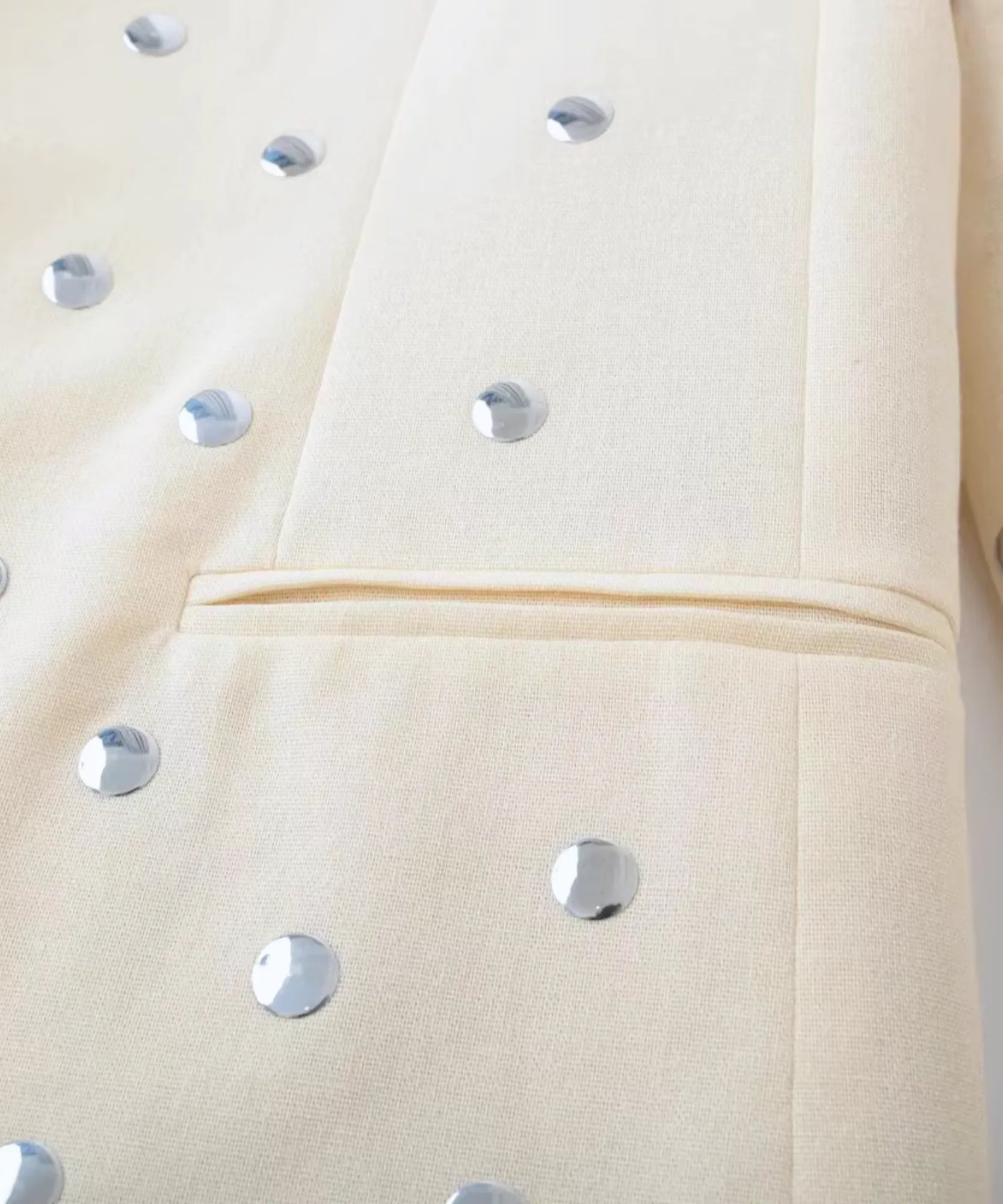 Detalhe das tachas metalizadas no bolso e na manga do blazer bege feminino
