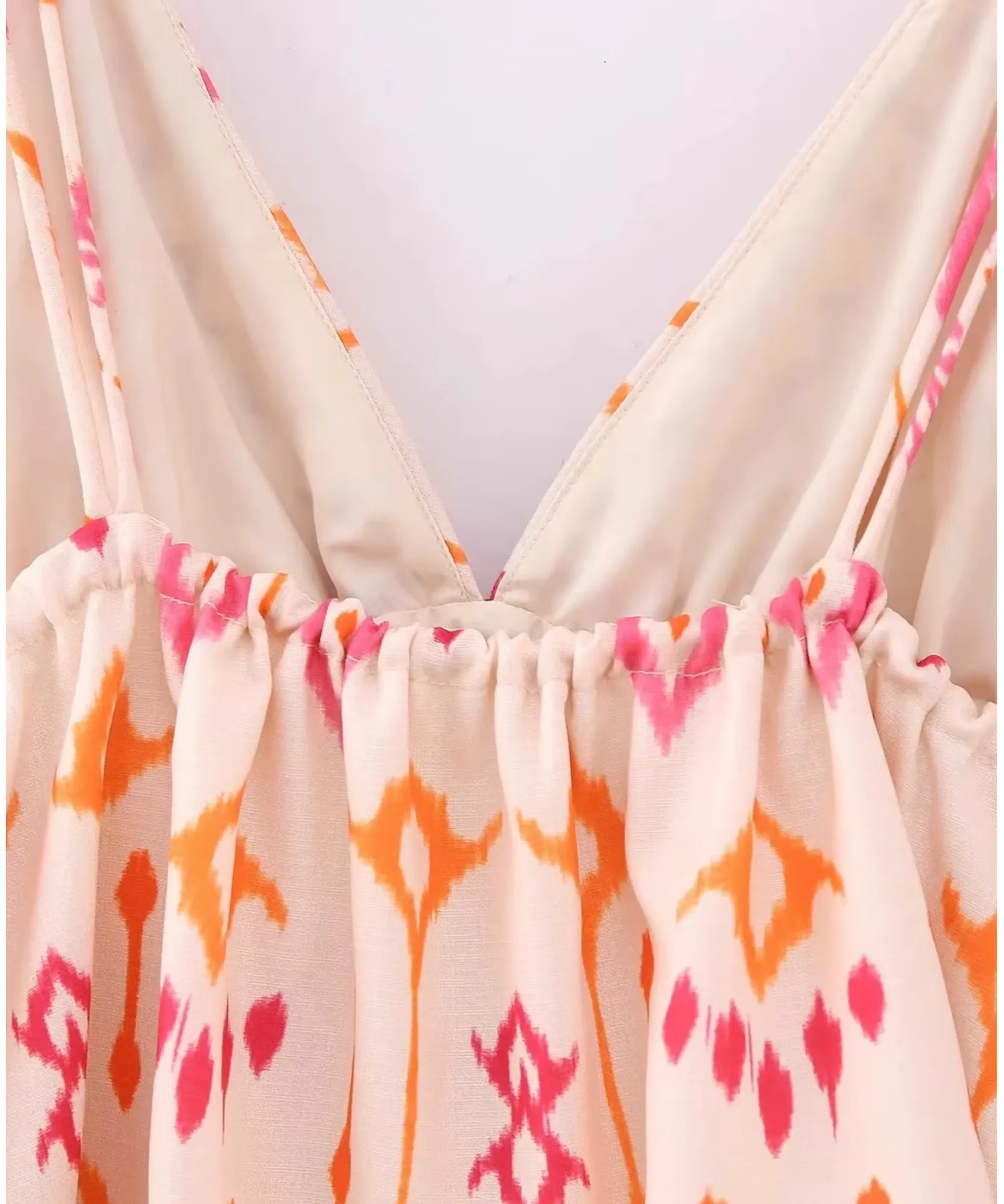 Detalhe das alças finas reguláveis e do decote da blusa cropped boho bege com estampa rosa e laranja