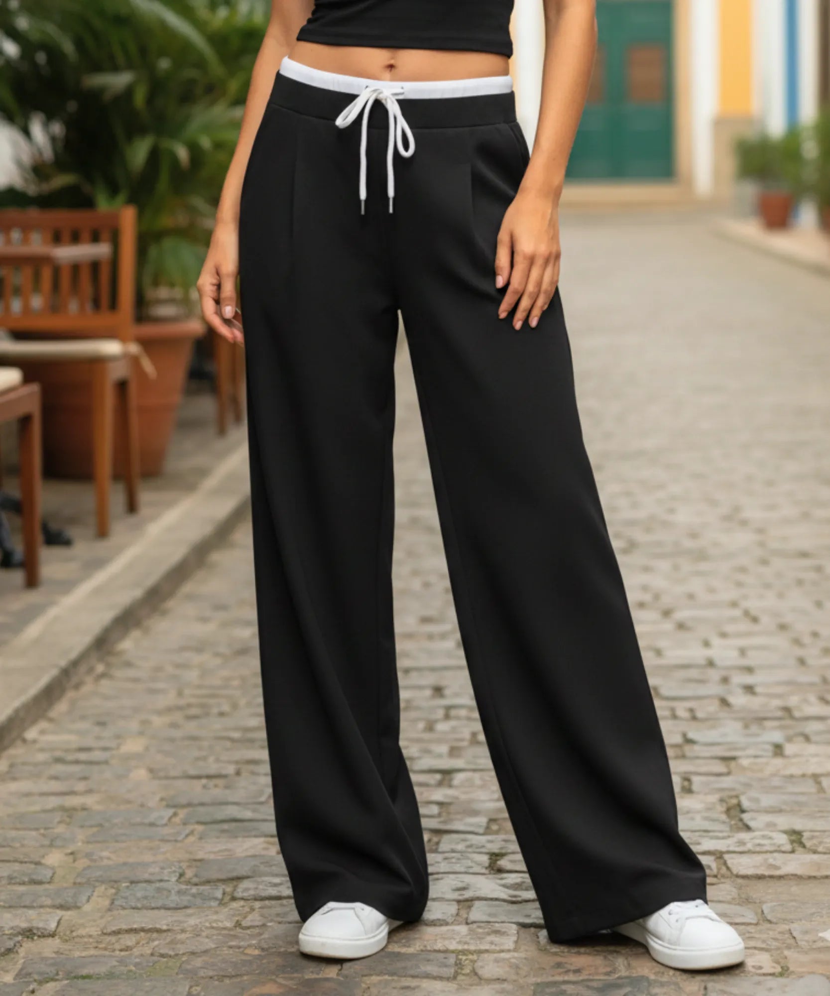 Calça alfaiataria wide leg preta com barra reta cobrindo o tênis branco