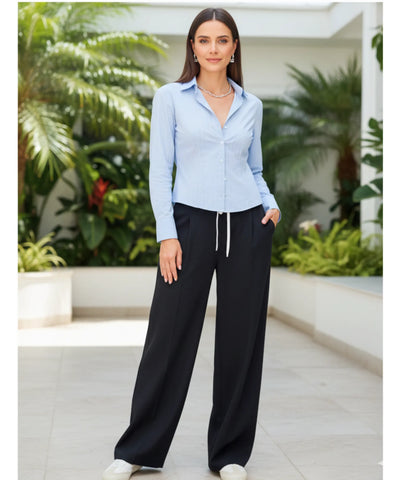Modelo de corpo inteiro usando calça alfaiataria wide leg preta com elástico na cintura e camisa azul claro