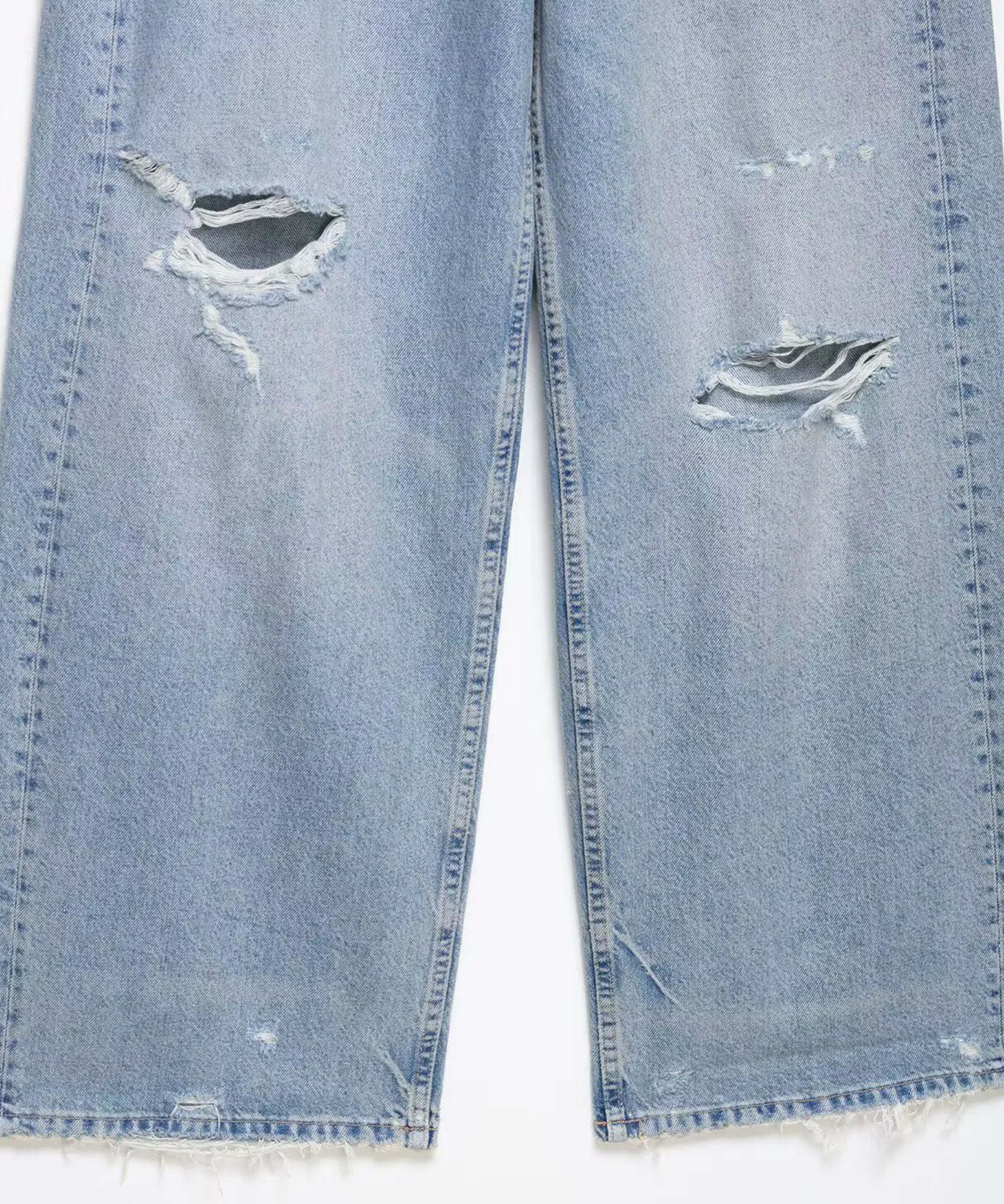 Detalhe dos rasgos no joelho e da barra desfiada da calça baggy azul claro