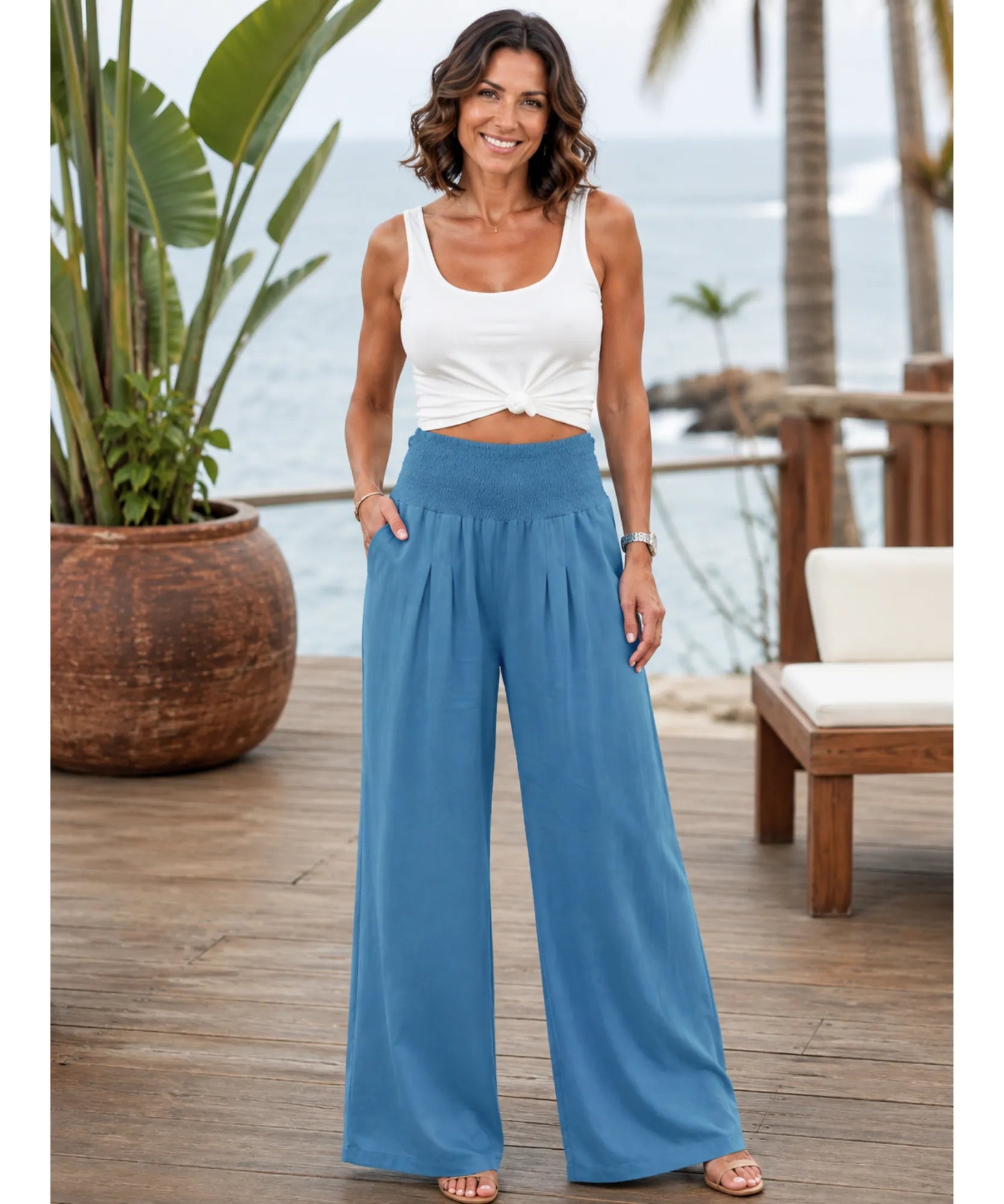 Calça pantalona feminina fluida azul com cós franzido elástico, vista de corpo inteiro na modelo em cenário de praia