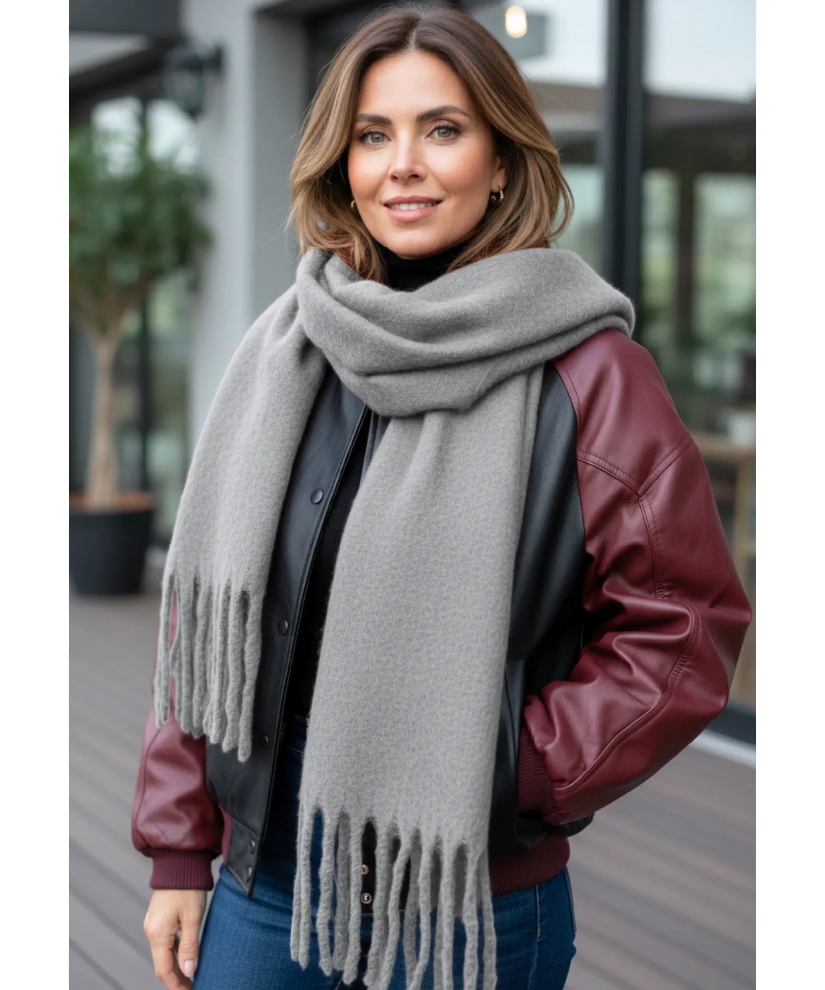 Woman wearing a long, thick gray scarf with fringes, paired with a burgundy leather jacket.