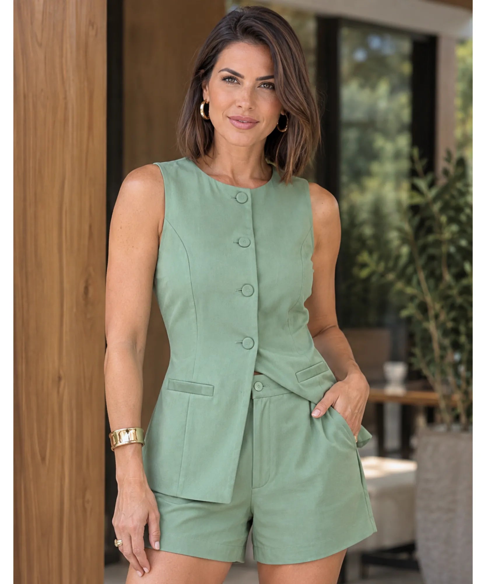 Conjunto alfaiataria feminino colete e short verde oliva, modelo vestindo de frente com as mãos nos bolsos
