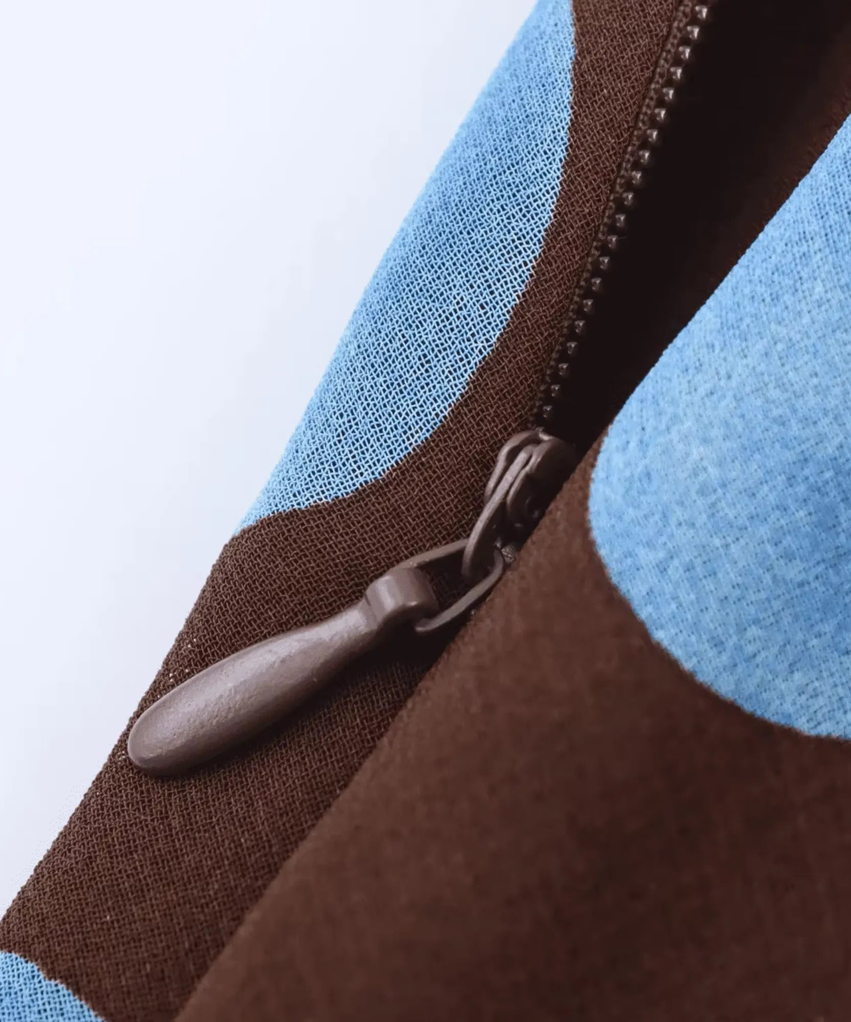 Macro do zíper lateral da saia midi poá marrom, com dentes na cor do tecido e poá azul ao lado