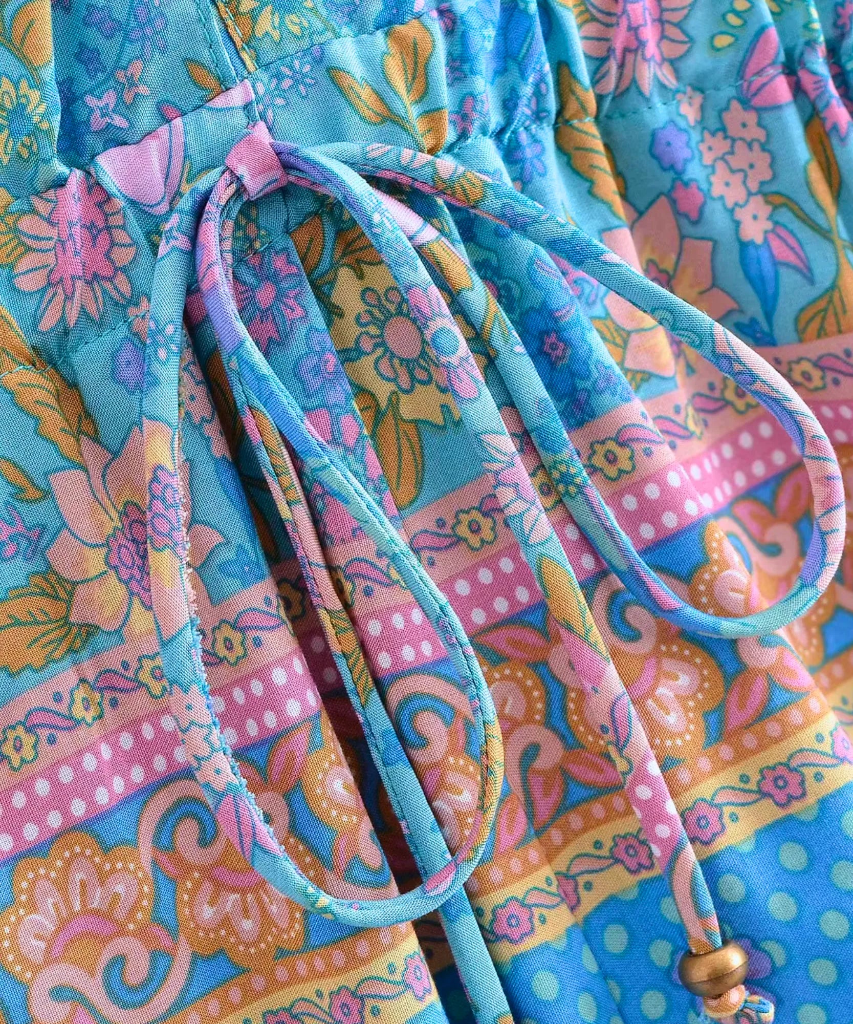 Detalhe do cordão de ajuste na cintura com ponteiras metalizadas do macaquinho feminino azul