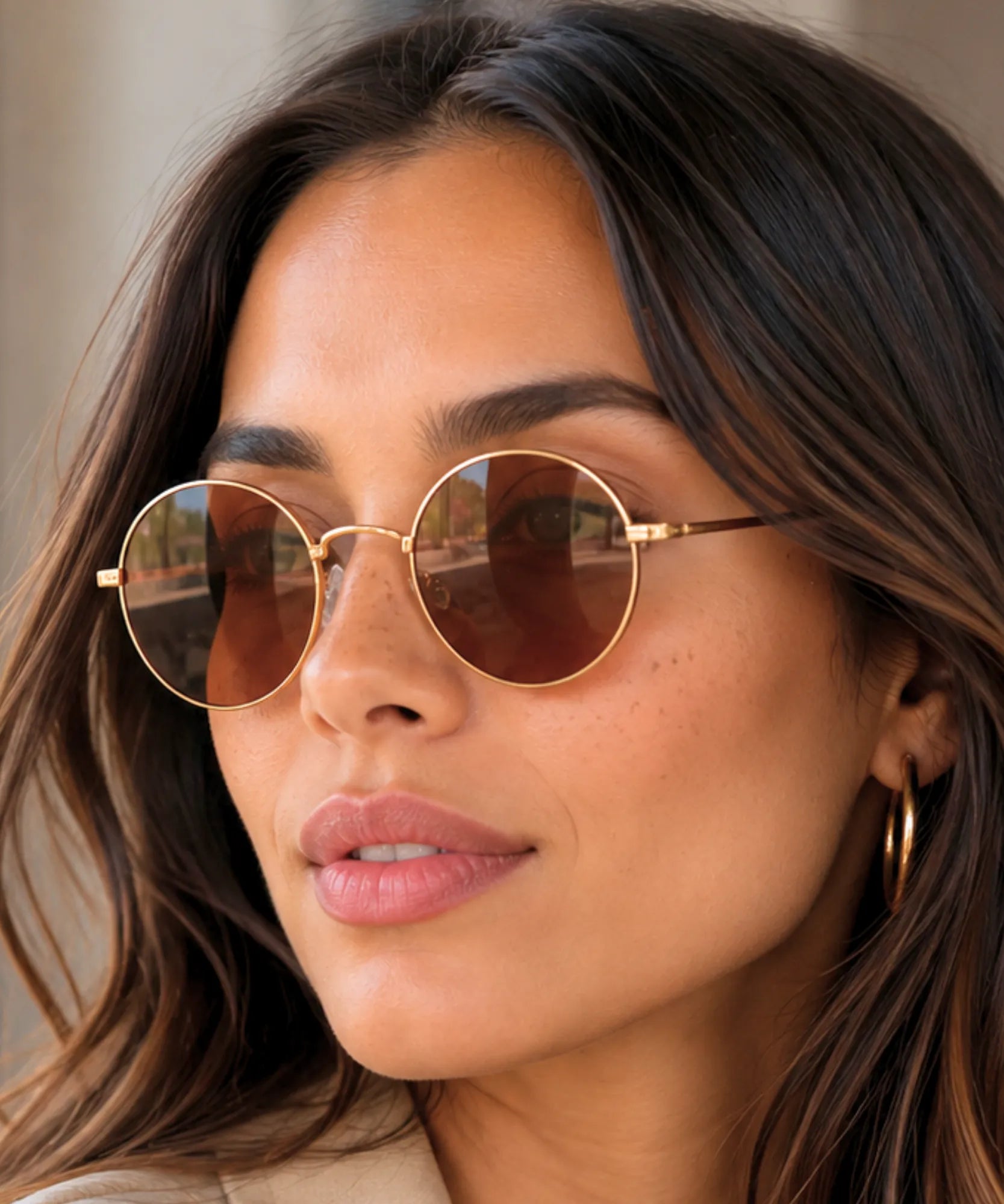Óculos de sol redondo vintage feminino com armação dourada e lente café em close no rosto da modelo | Allore Anellimn