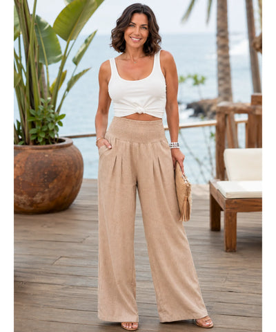 Calça pantalona feminina fluida em bege dourado, vista de corpo inteiro na modelo em cenário de praia