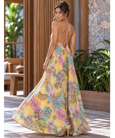 Vestido longo floral amarelo com alças finas cruzadas nas costas, modelo caminhando